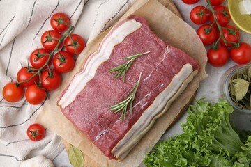 Piece of raw beef meat, tomatoes and spices on grey table, flat lay