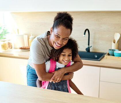 Mother helping daughter to get ready for school, helping her with backpack and books, and making snack sandwich in the kitchen hugging and leaving home - Powered by Adobe