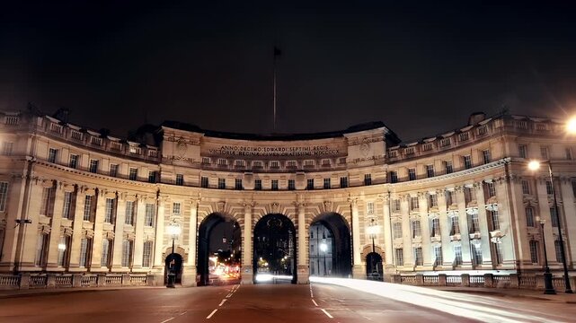 Admiralty Arch. London, United Kingdom. A nighttime cityscape featuring a grand building with a clock tower. The buildings facade is illuminated, revealing a series of windows. The sky is dark.