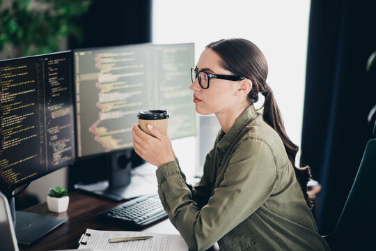 Young female programmer working in a modern workspace with coding on monitors and a coffee cup in a casual style