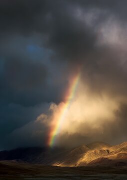 A stunning rainbow arcs through dramatic clouds and mountains, contrasting vibrant colors with a moody sky, creating an enchanting natural scene