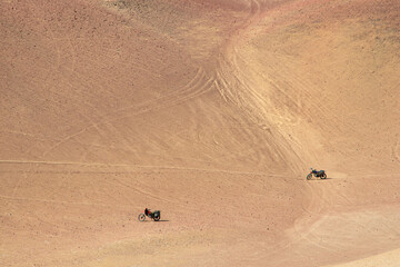 Two motorcycles ride across a vast, sandy desert landscape in Peru under a clear sky, evoking...