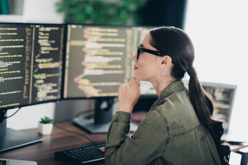 Professional computer programmer analyzing code on multiple monitors in a modern office workspace setting