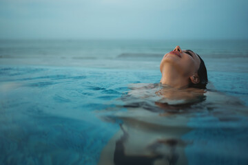 beautiful woman swimming in luxury pool at sunset flowing into sea, elegant vacation and tropical serenity, stunning girl relaxing in lavish resort pool at sunrise