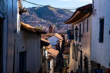 Enge Gasse in Cusco mit Dächern und Kirchturm im Vordergrund und der Stadt am Berghang im...