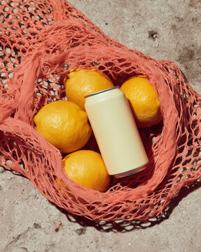 An aluminum can with lemonade lying in a mesh bag with ripe lemons. Refreshing drinks.
