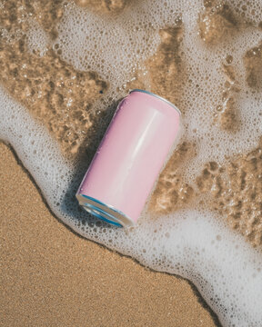 A pink aluminum can lying on the sandy beach shore. Refreshing drinks on a hot day.