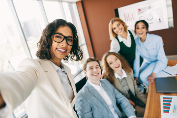 Work colleagues taking a cheerful team selfie in a modern office during a collaborative business meeting