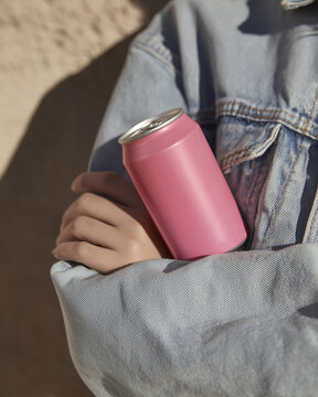 A girl in a denim jacket holding a pink aluminum soda can between her hands. Refreshing chilled drinks.