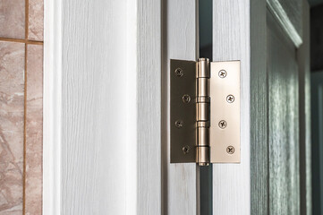 Metal door hinge on open white wooden door.