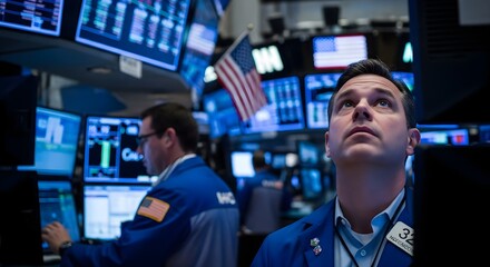 A man in a blue suit looks up intently on a financial trading floor, surrounded by multiple glowing data screens and an American flag.