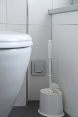close-up view of a sleek white toilet with a matching toilet brush holder and brush positioned next...