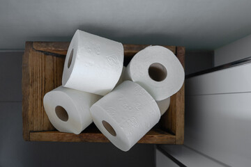 top view of four neatly stacked rolls of white toilet paper in a rustic wooden basket against a soft gray wall, highlighting essential bathroom supplies and aesthetic organization
