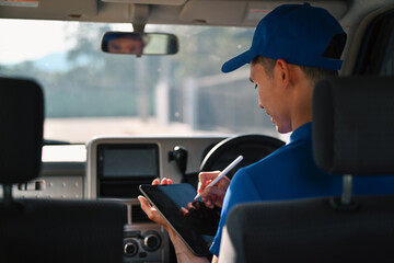 A Rear view shot of a courier inside a delivery van using a digital tablet and stylus to log package details