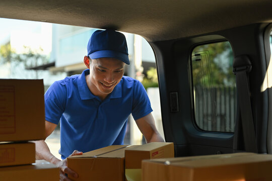 Smiling worker sorts parcels in the cargo space of a delivery van, ready for distribution in a residential area