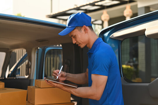 A Focused Asian deliveryman in a blue uniform using a digital tablet to check and record packages during delivery, Digital Package Management for Modern Delivery Services