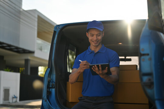 Deliveryman managing packages on a digital tablet at the back of a van with sunlight shining