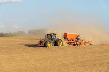 Obraz premium A tractor towing a seeder creates dust clouds while performing field work