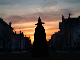 Fototapeta premium Silhouette of a Witch in a Cityscape During Sunset, Mysterious and Eerie Scene