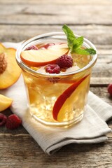 Iced tea. Refreshing drink with peach and raspberries in glass on wooden table, closeup