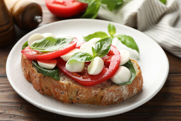 Delicious sandwich with mozzarella cheese, tomatoes and basil on wooden table, closeup