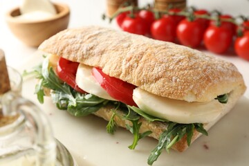 Delicious sandwich with mozzarella cheese, tomatoes and arugula on table, closeup