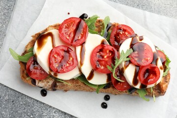 Delicious sandwich with mozzarella cheese, balsamic sauce, tomato and arugula on grey table, top view