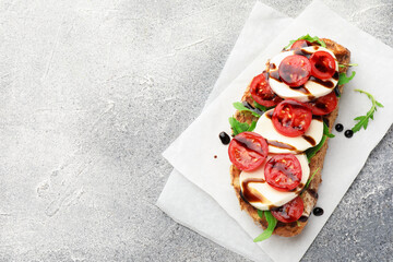 Delicious sandwich with mozzarella cheese, balsamic sauce, tomato and arugula on grey table, top view. Space for text