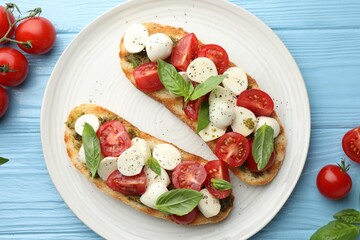 Delicious sandwiches with mozzarella cheese, tomatoes and basil on light blue wooden table, flat lay
