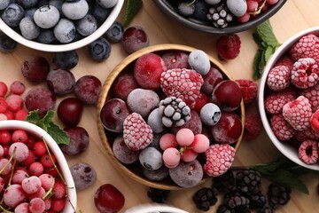Different ripe frozen berries and mint leaves on light wooden table, flat lay