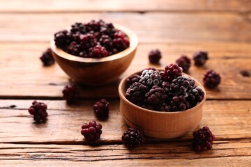 Ripe frozen blackberries in bowls on wooden table, closeup