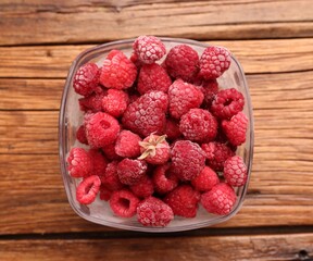 Ripe frozen raspberries in bowl on wooden table, top view