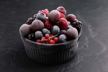 Mix of ripe frozen berries in bowl on dark textured table, closeup