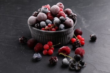 Mix of ripe frozen berries and bowl on dark textured table, closeup