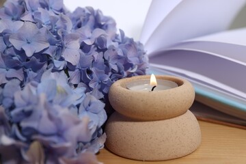 Spa composition with burning candle, beautiful hydrangea flowers and book on wooden table, closeup