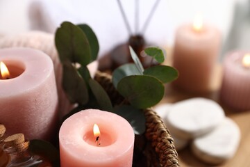 Spa composition. Burning candles, cosmetic products and eucalyptus branches in basket on table, closeup