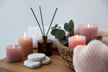 Spa composition with burning candles and reed air freshener on wooden table indoors, closeup