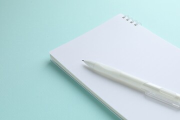 White notebook and pen on light blue background, closeup. Space for text