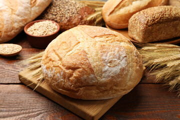 Loaves of fresh bread, grains and wheat spikes on wooden table, closeup