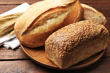 Loaves of fresh bread and wheat spikes on wooden table, closeup