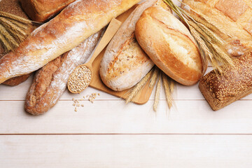 Different types of bread, grains and wheat spikes on wooden table, flat lay. Space for text