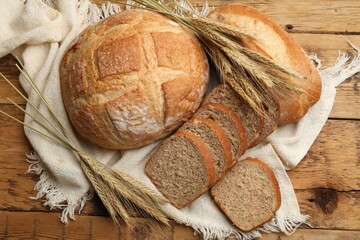Different types of bread and wheat spikes on wooden table, flat lay