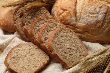 Different types of bread and wheat spikes on table, closeup