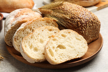 Different types of bread and wheat spikes on grey table, closeup