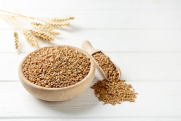 Wheat grains in bowl, scoop and spikelets on white wooden table, closeup. Space for text