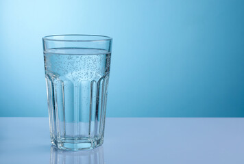 Refreshing soda water in glass on white mirror table against light blue gradient background, closeup. Space for text