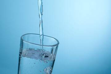 Pouring refreshing soda water into glass against light blue gradient background, closeup. Space for text