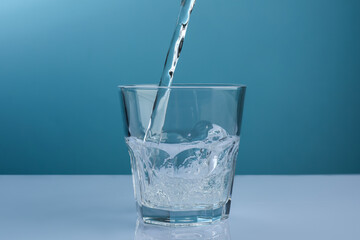 Pouring refreshing soda water into glass at white mirror table against light blue background, closeup