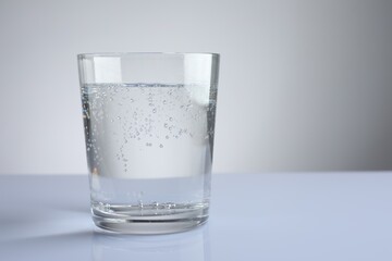 Refreshing soda water in glass on white mirror table against grey gradient background, closeup. Space for text