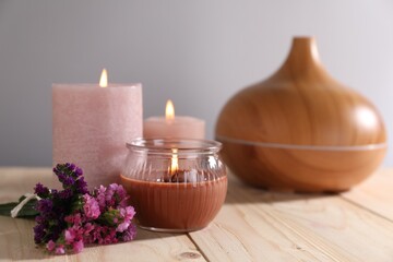 Spa composition with flowers and burning candles on wooden table against grey background, closeup